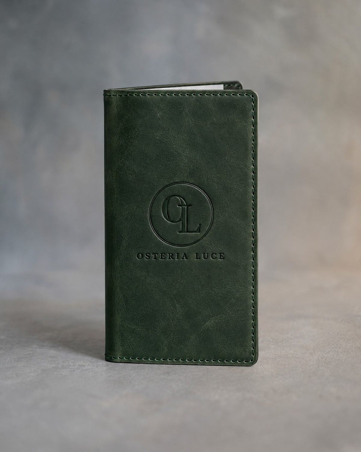 Forest Green leather check presenter debossed with a sample business logo on the front, on a grey plaster backdrop