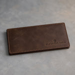 Dark Espresso leather checkbook cover debossed with a sample business logo, on a grey plaster backdrop