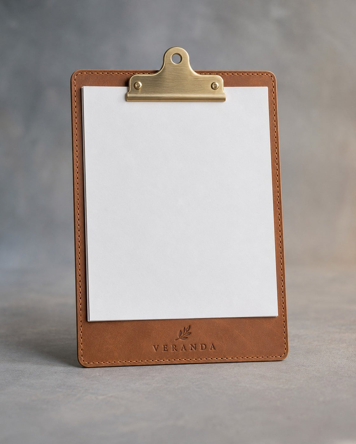 Caramel leather clipboard with brass clip, debossed with a sample business logo, on a grey plaster backdrop