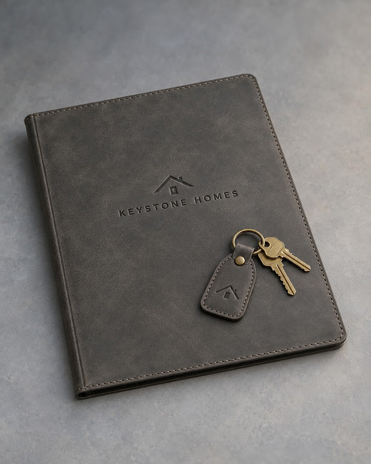 Country Gray leather closing folder and keychain debossed with a sample business logo, on a grey plaster backdrop