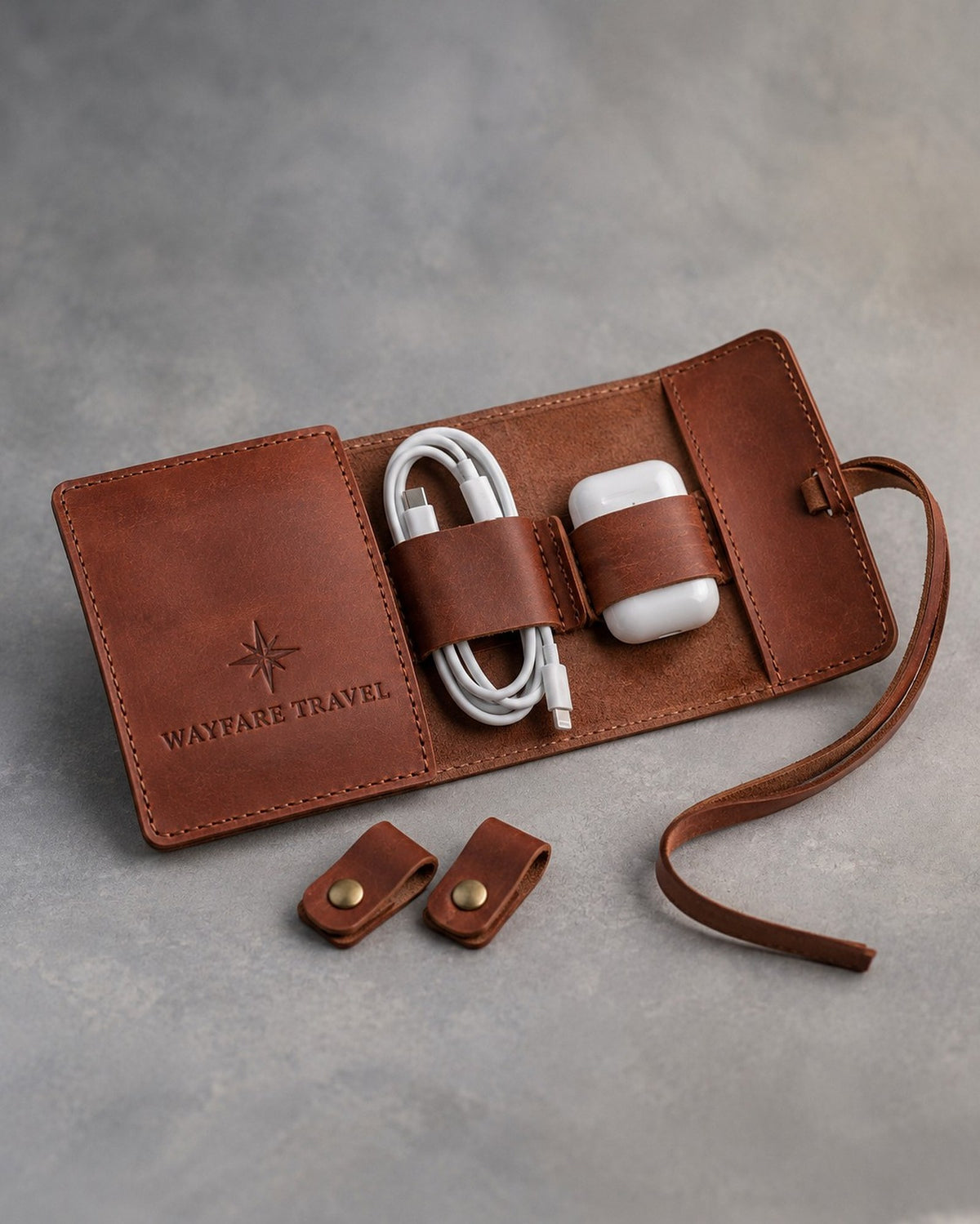 Arizona leather cord organizer roll with cord keepers, debossed with a sample business logo, on a grey plaster backdrop