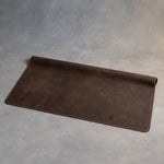 Dark Espresso leather desk mat debossed with a sample business logo in the corner, on a grey plaster backdrop