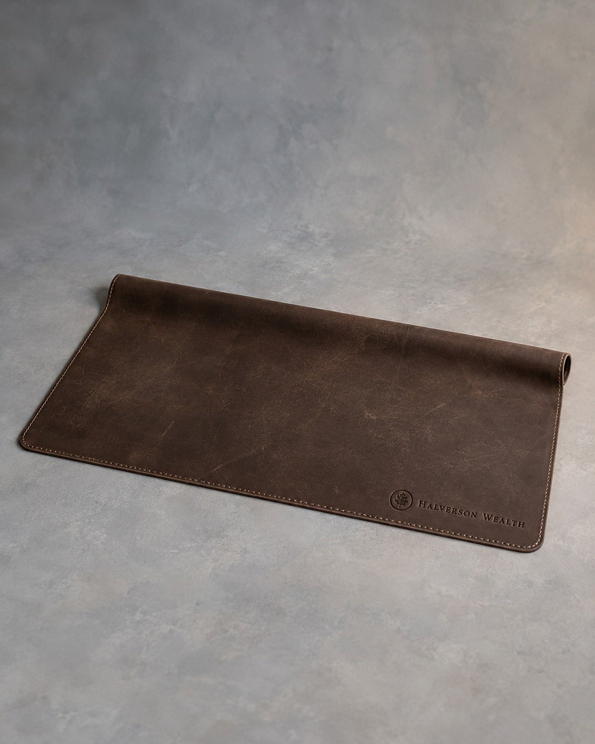 Dark Espresso leather desk mat debossed with a sample business logo in the corner, on a grey plaster backdrop