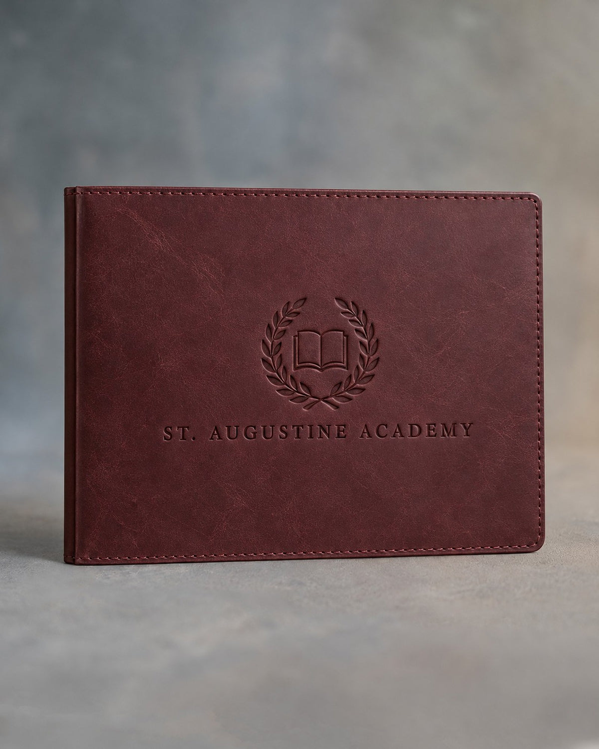 Sangria leather diploma cover debossed with a sample business logo, on a grey plaster backdrop