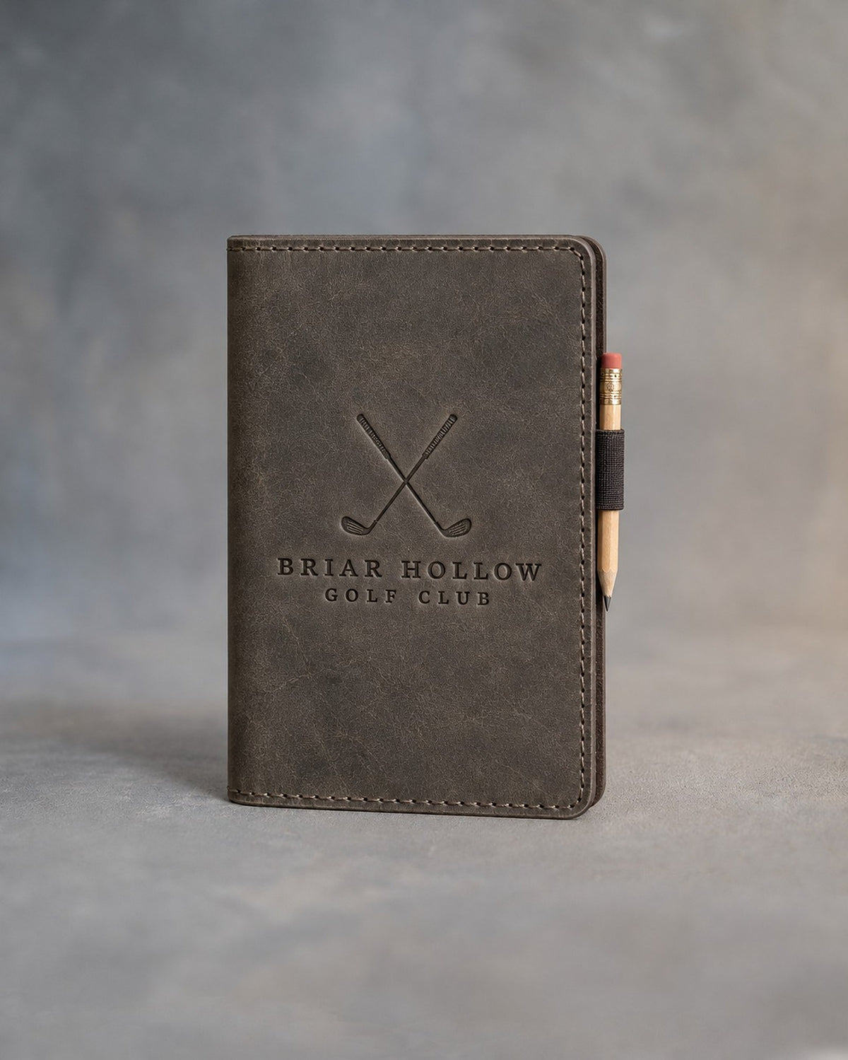 Country Gray leather golf scorecard holder debossed with a sample business logo, on a grey plaster backdrop