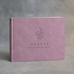 Lilac padded leather guest book in landscape format, debossed with a sample business logo, on a grey plaster backdrop