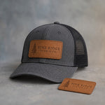Caramel leather hat patch with stitched edge debossed with a sample business logo, on a grey plaster backdrop