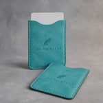 Turquoise leather hotel key card sleeve debossed with a sample business logo, on a grey plaster backdrop