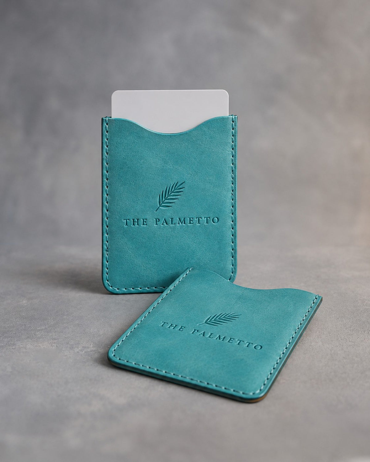 Turquoise leather hotel key card sleeve debossed with a sample business logo, on a grey plaster backdrop