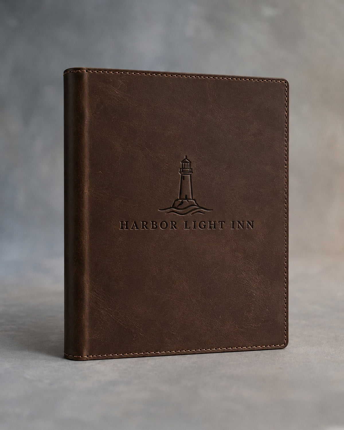Dark Espresso leather hotel room directory debossed with a sample business logo, on a grey plaster backdrop