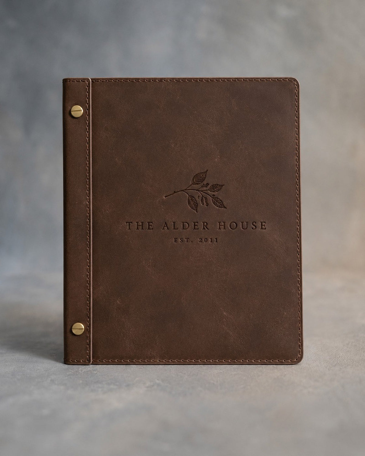 Sicilian Brown leather menu cover debossed with a sample business logo on the front, on a grey plaster backdrop