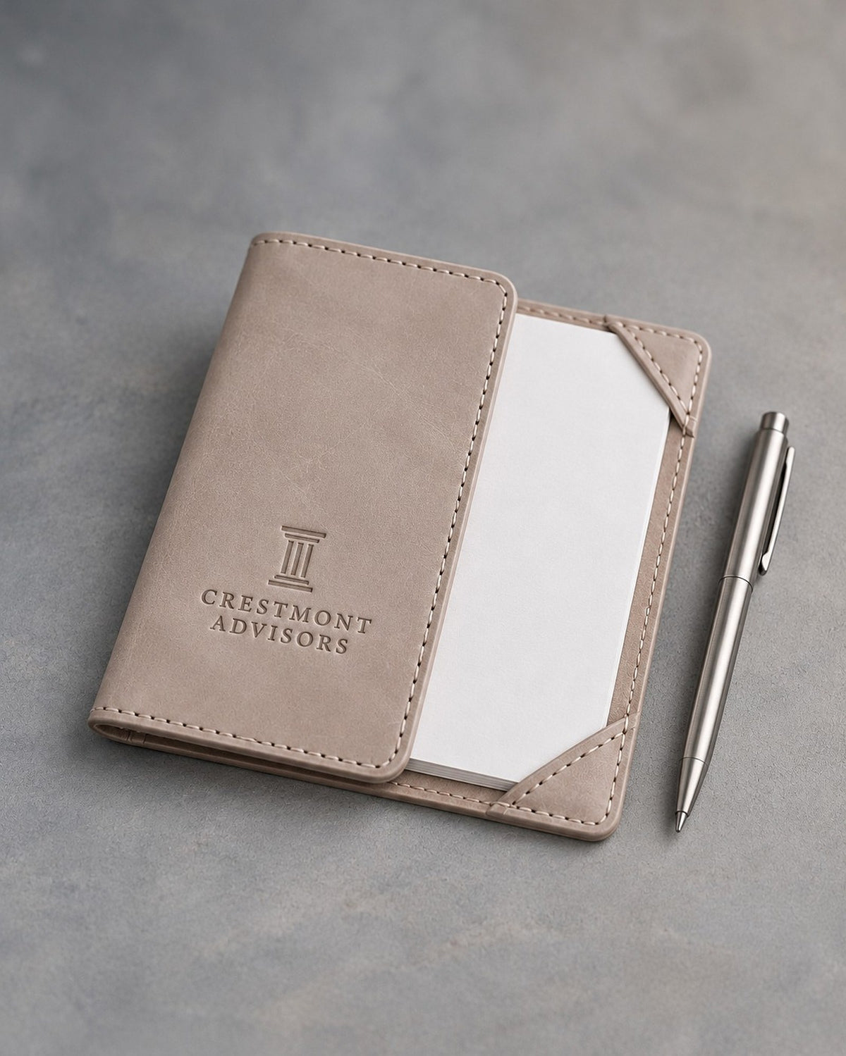 Gray Sand leather notepad holder debossed with a sample business logo, on a grey plaster backdrop