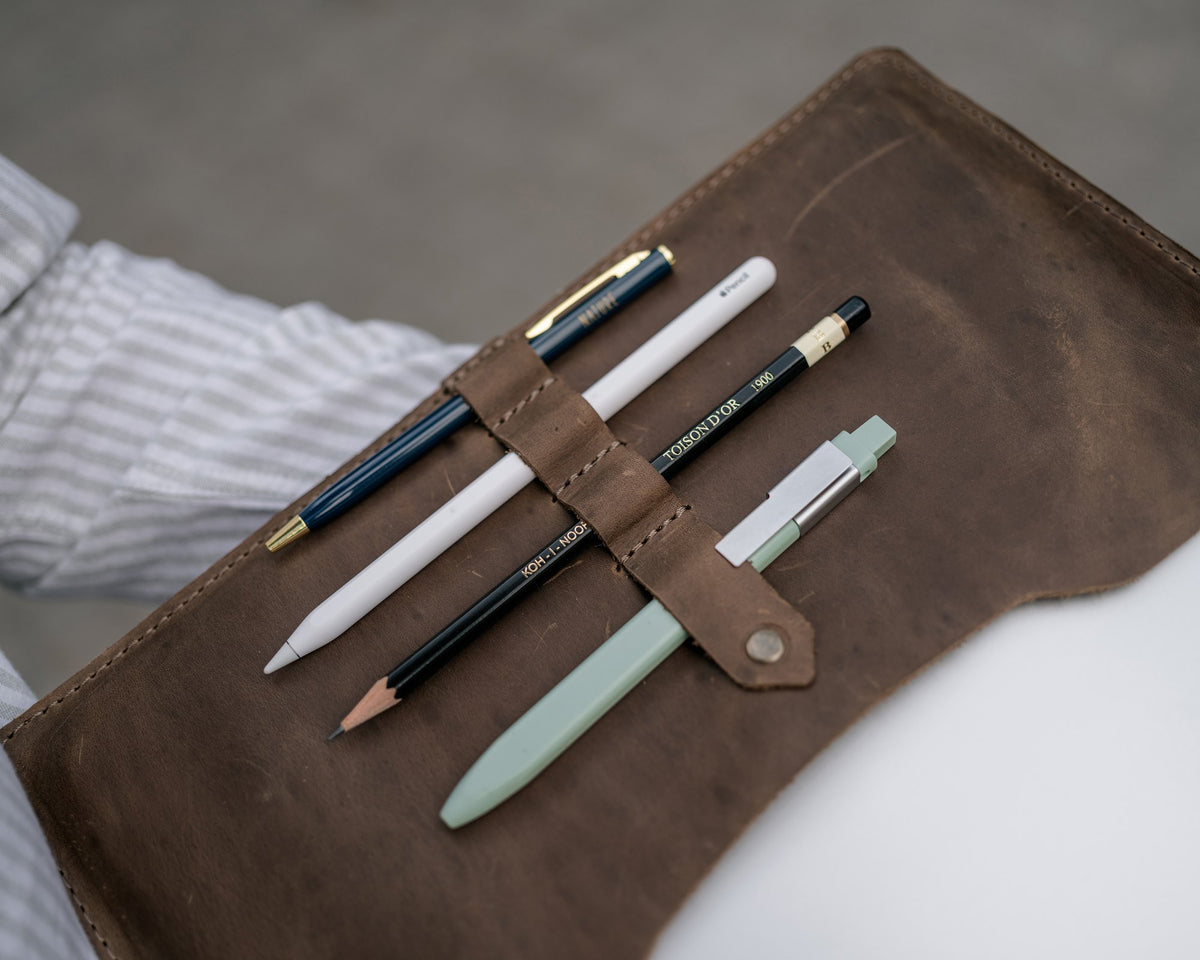 Snap pen strap inside the leather padfolio holding four pens, close up
