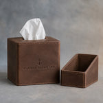 Sicilian Brown leather tissue box cover with oval top opening, debossed with a sample business logo, on grey plaster
