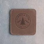 Sicilian Brown square leather coaster debossed with a sample round company logo, stitched edge, on grey plaster