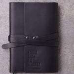 Black leather wrap journal debossed with the Olive Tree People logo, seen from above