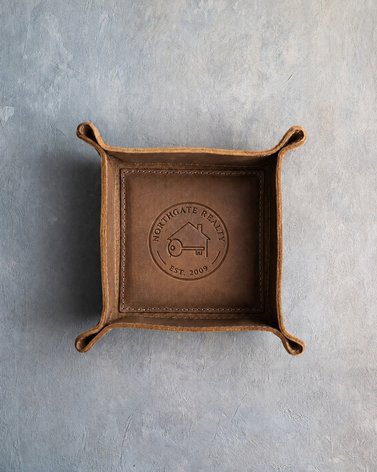 Sicilian Brown leather valet tray with a sample realty logo, NORTHGATE REALTY EST. 2009, pressed into the base, on grey plaster