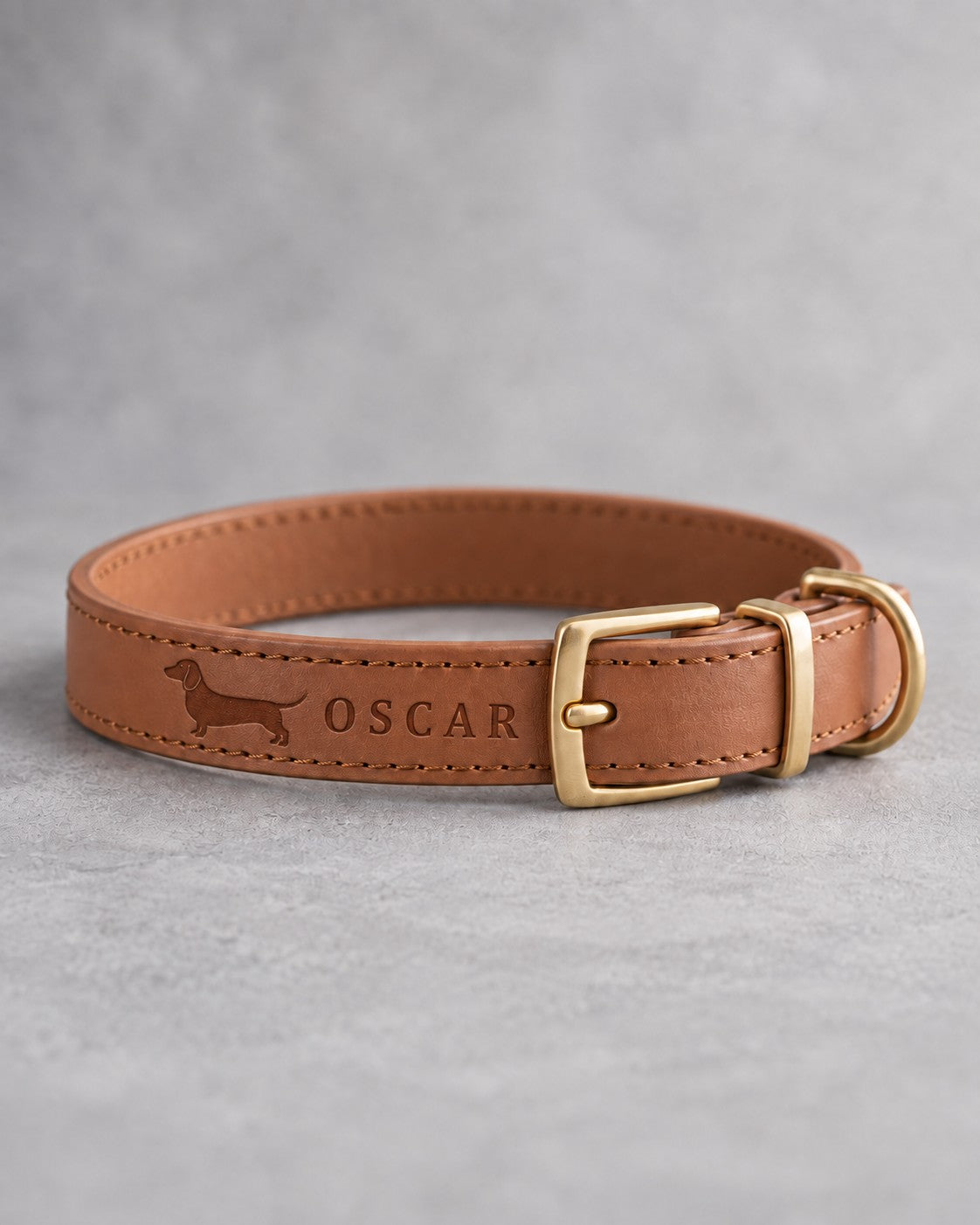Caramel leather dog collar with a dachshund silhouette and the name OSCAR debossed beside a brass pin buckle
