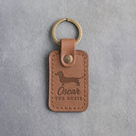 Caramel leather keychain with a dachshund silhouette and the name Oscar above THE DOXIE, debossed, on gray concrete