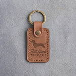 Caramel leather keychain with a dachshund silhouette above Best friend and THE DOXIE, debossed, on gray concrete