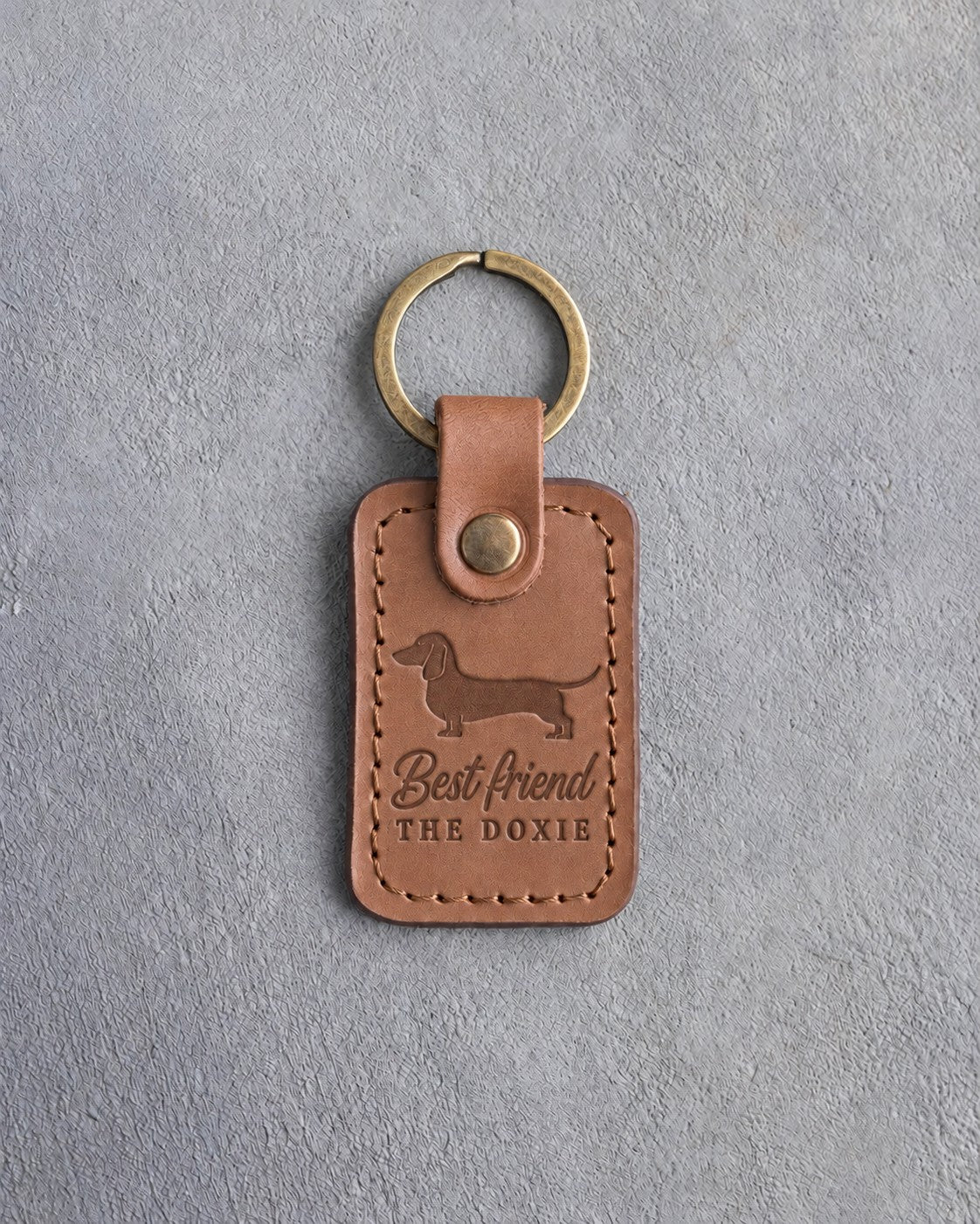 Caramel leather keychain with a dachshund silhouette above Best friend and THE DOXIE, debossed, on gray concrete