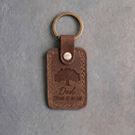 Sicilian brown leather keychain debossed with a solid oak tree above Dad and STRONG AS AN OAK, on gray concrete