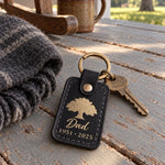 Black Dad memorial keychain with gold lettering held in an open palm in soft window light