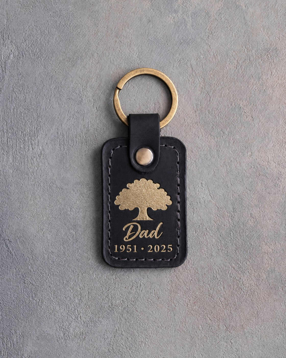 Black leather keychain with a gold foil oak tree above Dad and 1951 · 2025
