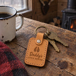 Daddy's Little Hunter keychain in golden tan leather held in a toddler's hand beside a tiny blaze orange cap