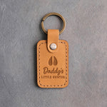 Golden tan leather keychain debossed with a small fawn track above the words Daddy's LITTLE HUNTER, on gray plaster