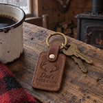 Dad's Deer Camp keychain in brown leather on a gate key hanging from a nail on a weathered cabin wall