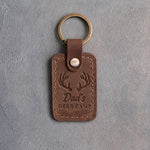 Sicilian brown leather keychain debossed with whitetail antlers above the words Dad's DEER CAMP, on gray plaster