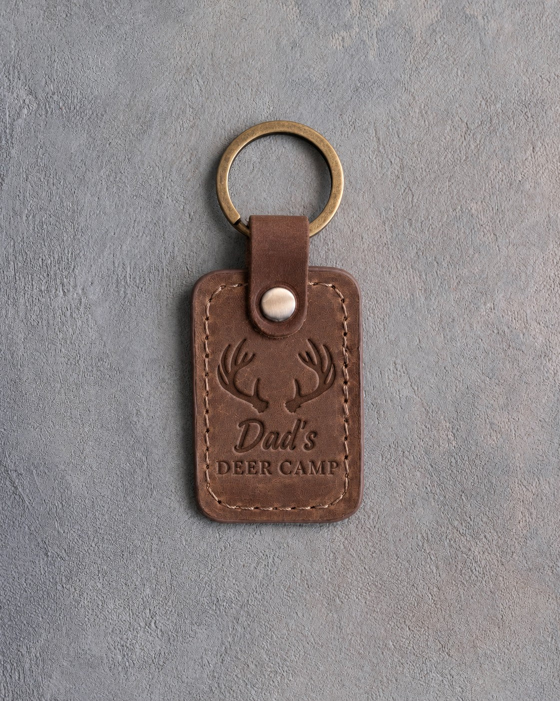 Sicilian brown leather keychain debossed with whitetail antlers above the words Dad's DEER CAMP, on gray plaster