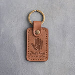 Caramel leather keychain debossed with a small hand inside a large hand above Dad's hugs and FIX ANYTHING