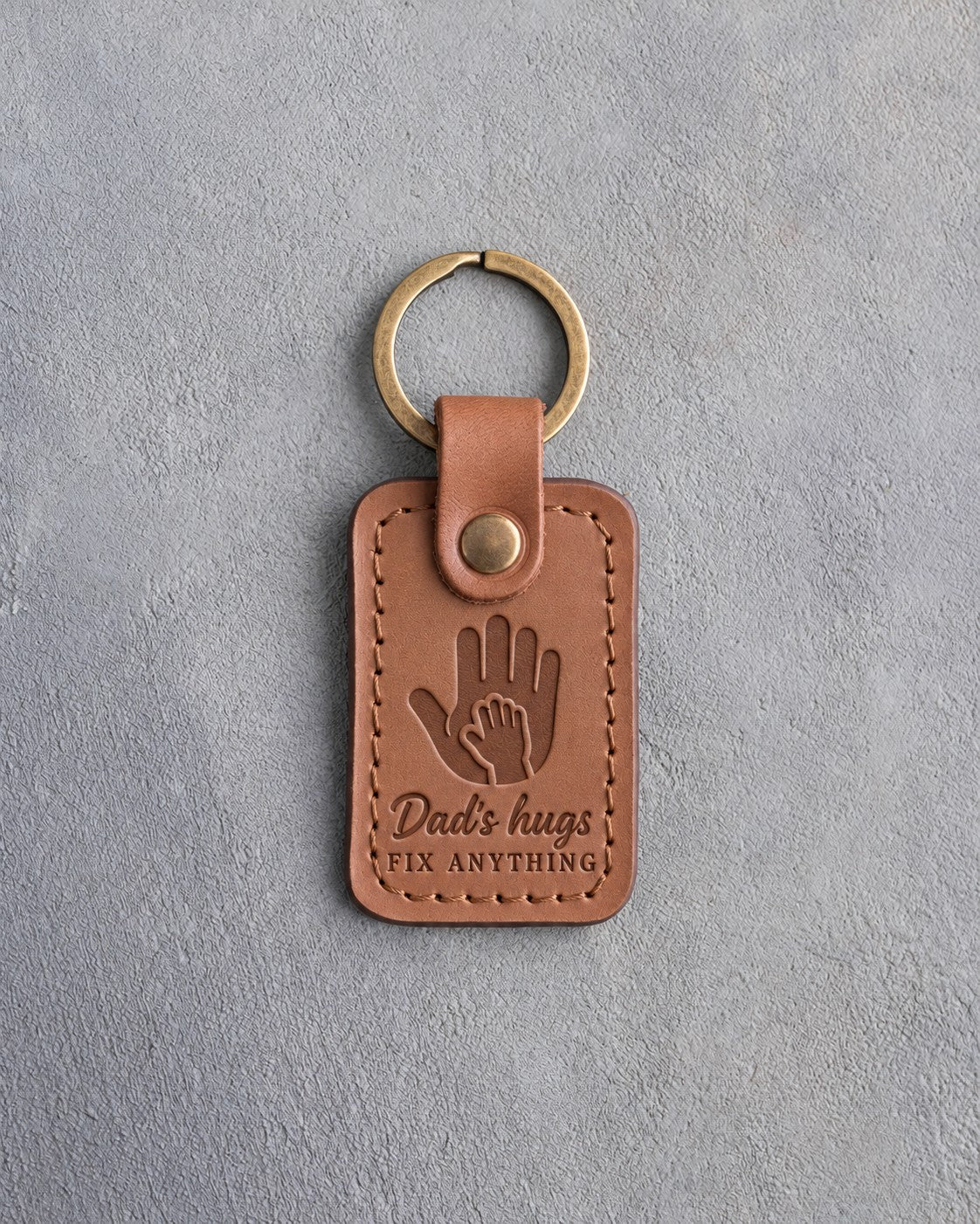 Caramel leather keychain debossed with a small hand inside a large hand above Dad's hugs and FIX ANYTHING