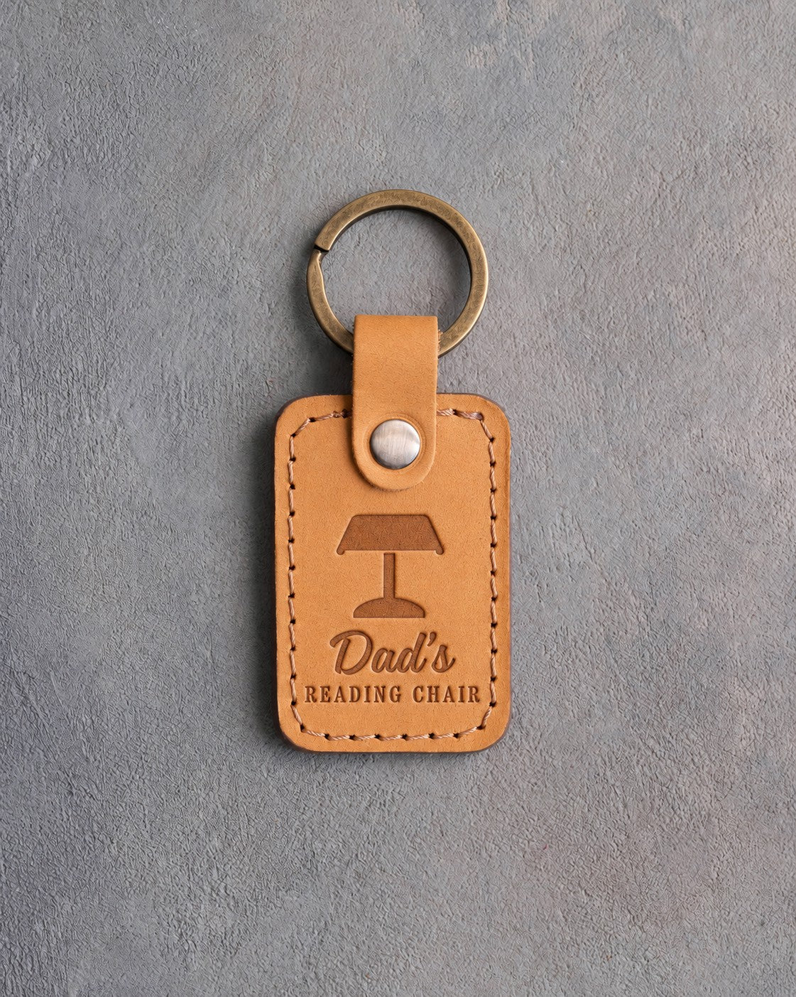 Indian Summer tan leather keychain debossed with a banker's lamp above Dad's and READING CHAIR, on gray concrete