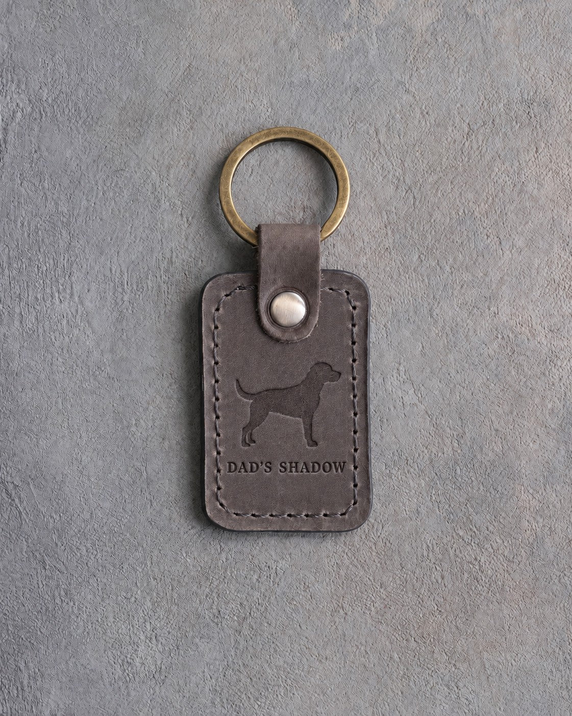 Country gray leather keychain debossed with a standing dog above DAD'S SHADOW, on gray concrete