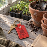 Red Dad's Tomatoes keychain on a garden fence post beside a vine heavy with ripe tomatoes