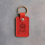 Poppy red leather keychain debossed with a ripe tomato above Dad's TOMATOES, on gray concrete