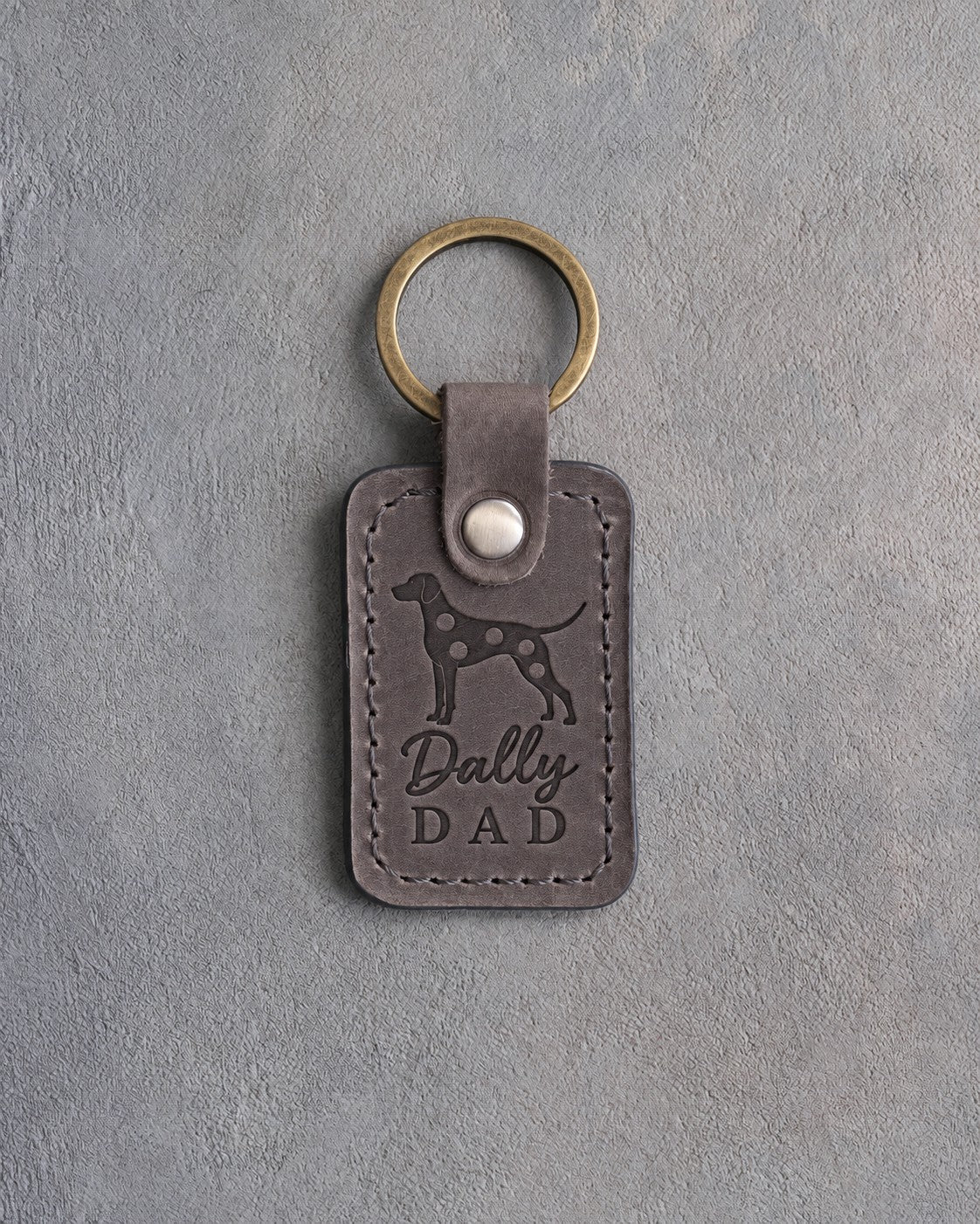 Country gray leather keychain debossed with a Dalmatian silhouette and the words Dally DAD, on gray concrete