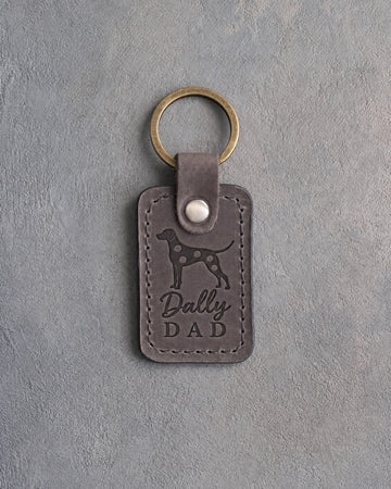 Country gray leather keychain debossed with a Dalmatian silhouette and the words Dally DAD, on gray concrete