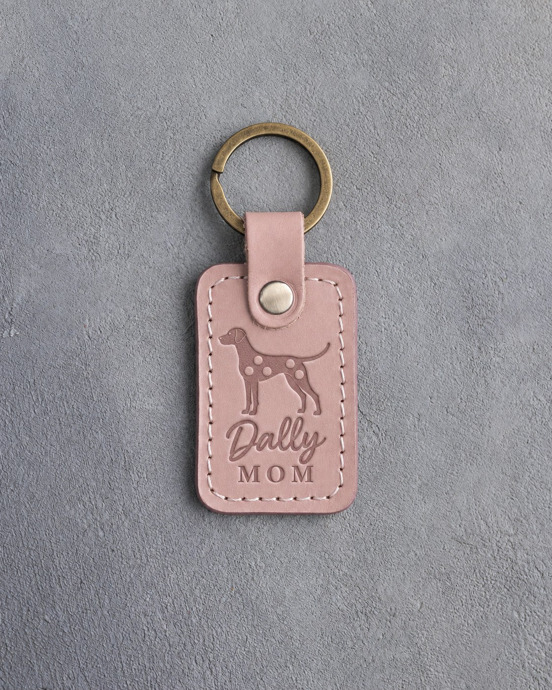 Blush pink leather keychain debossed with a Dalmatian silhouette and the words Dally MOM, on gray concrete
