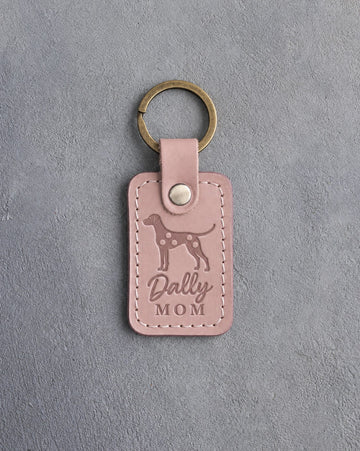 Blush pink leather keychain debossed with a Dalmatian silhouette and the words Dally MOM, on gray concrete
