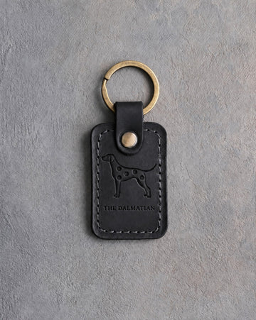 Black leather keychain debossed with a spotted Dalmatian silhouette above THE DALMATIAN, on gray concrete