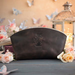 Dark espresso initial makeup pouch with a floral monogram, staged among pale roses on a slate table