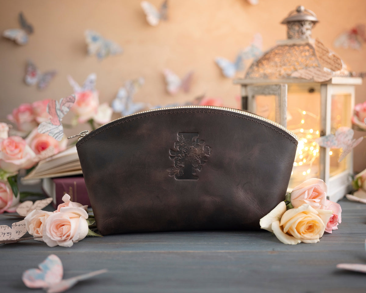 Dark espresso initial makeup pouch with a floral monogram, staged among pale roses on a slate table