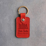 Poppy red leather keychain debossed with a shelf of books above Dear Santa and MORE SHELVES, on gray concrete