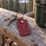 Deer Season Widow keychain in wine red leather on a kitchen counter beside a glass of red wine in evening lamplight