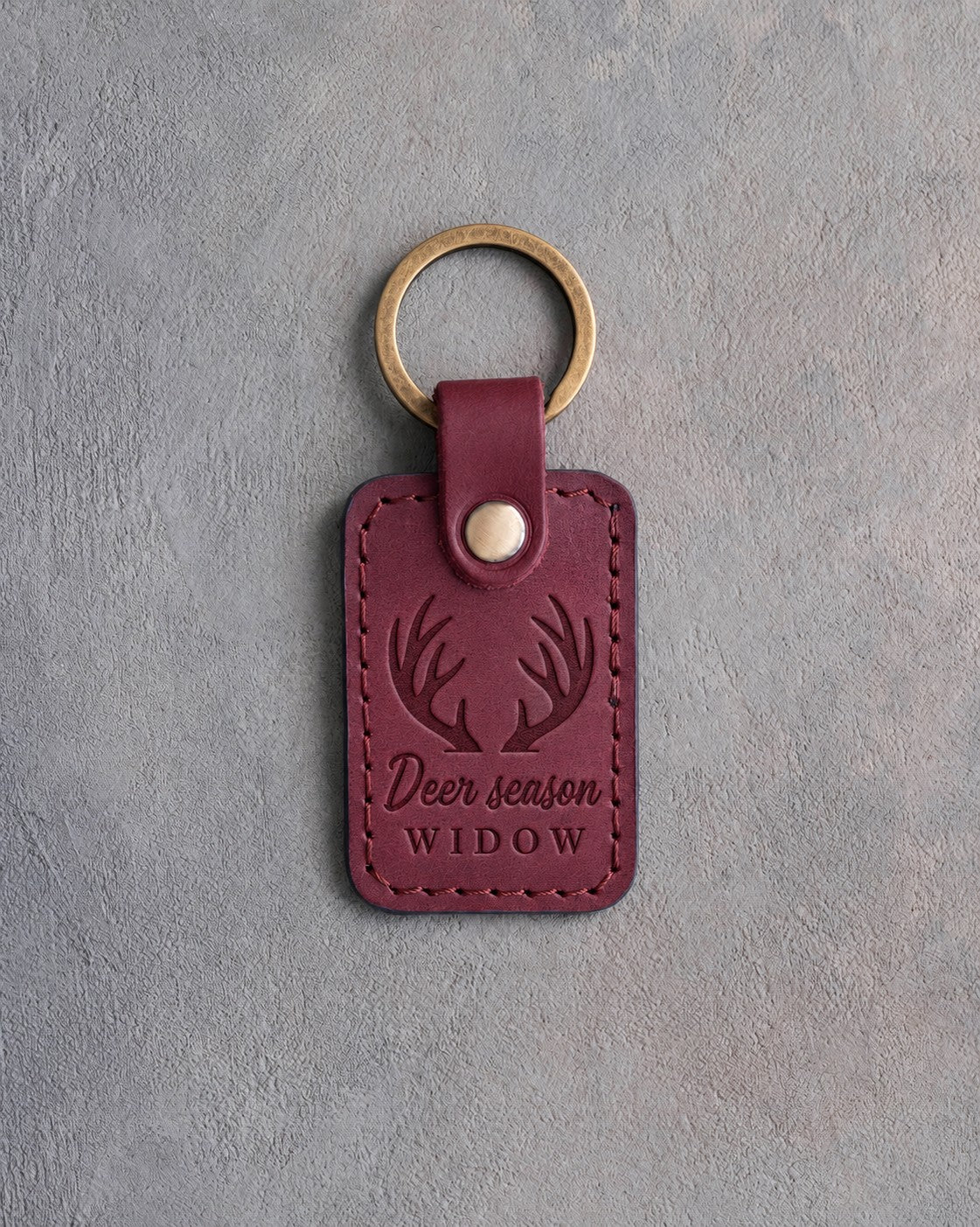 Sangria wine red leather keychain debossed with a front view of whitetail antlers above the words Deer season WIDOW, on gray plaster