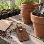 Dirt Therapy keychain in reddish brown leather on a potting bench beside a pair of worn garden gloves